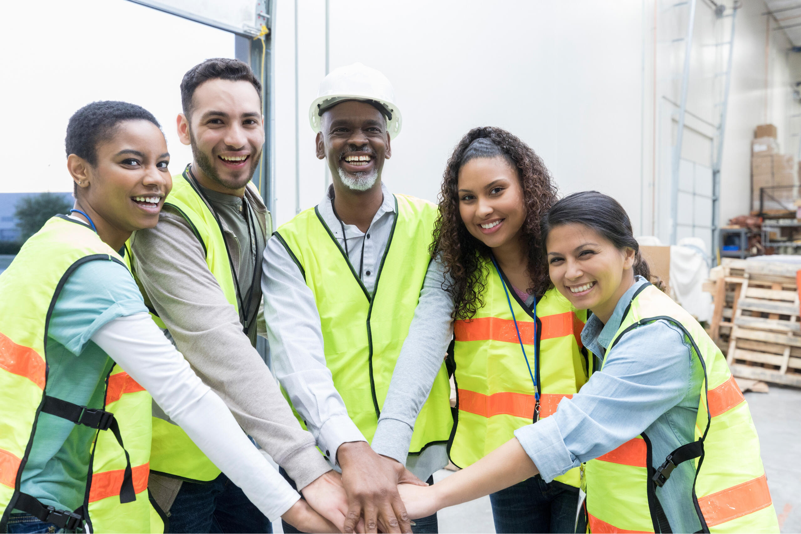 Team of warehouse employees smiling with their hands in for a group cheer